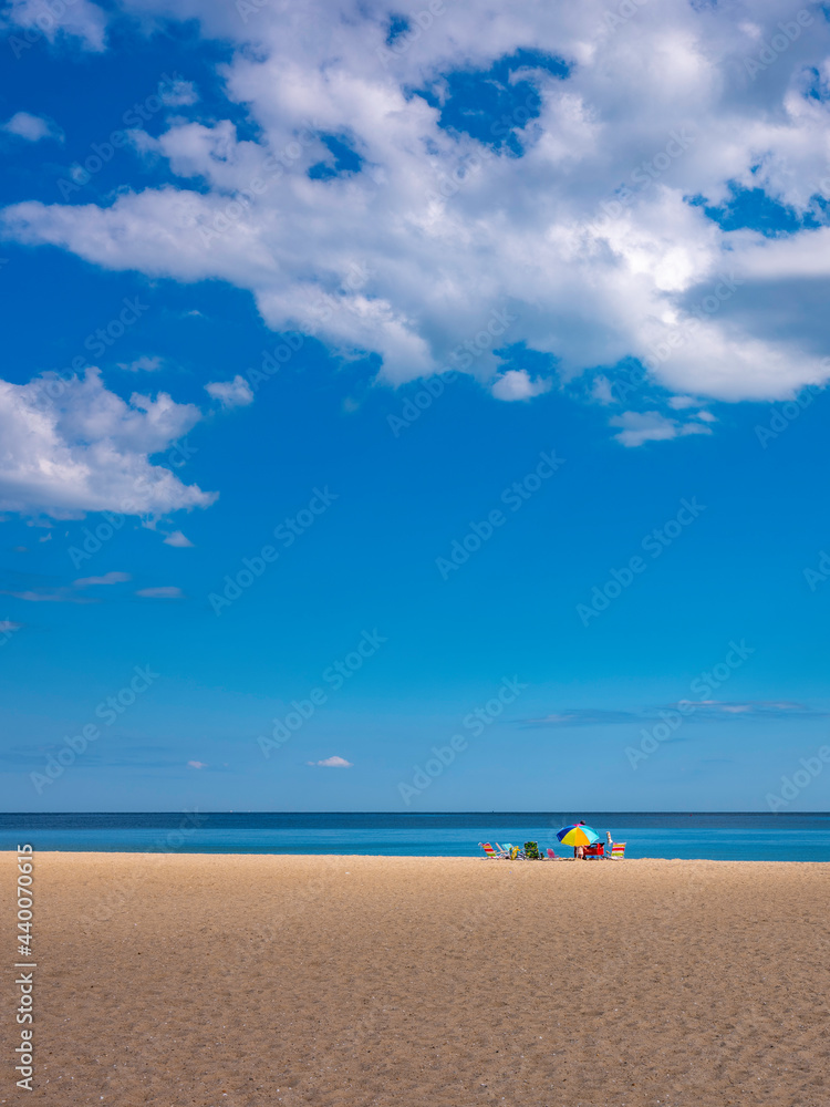 Beach seascape with a rainbow umbrella and beach chairs. Serene coastal landscape of family gathering. Peaceful summer ocean cloudscape on Cape Cod.  