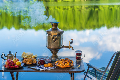 Slika na platnu Vintage metal tea samovar with white smoke and food on the table near the calm w