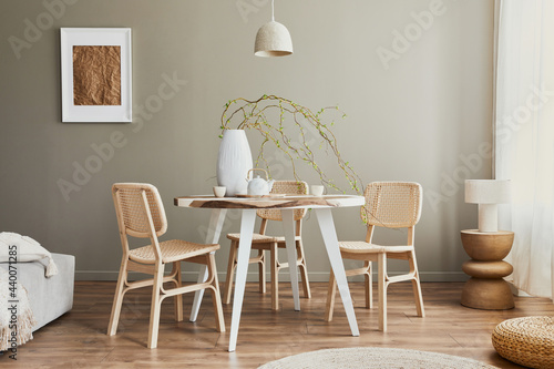 Stylish interior of dining room at cozy home with white mock up poster frame, design chairs, family table, teapot, cups, decoration and elegant personal accessories in modern home decor. Template. photo