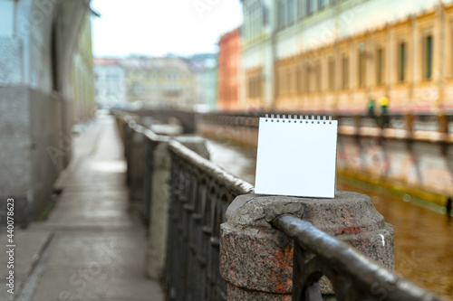 An empty white notebook with space for text stands on the embankment of the Neva River canal in St. Petersburg, mock up © KseniaJoyg