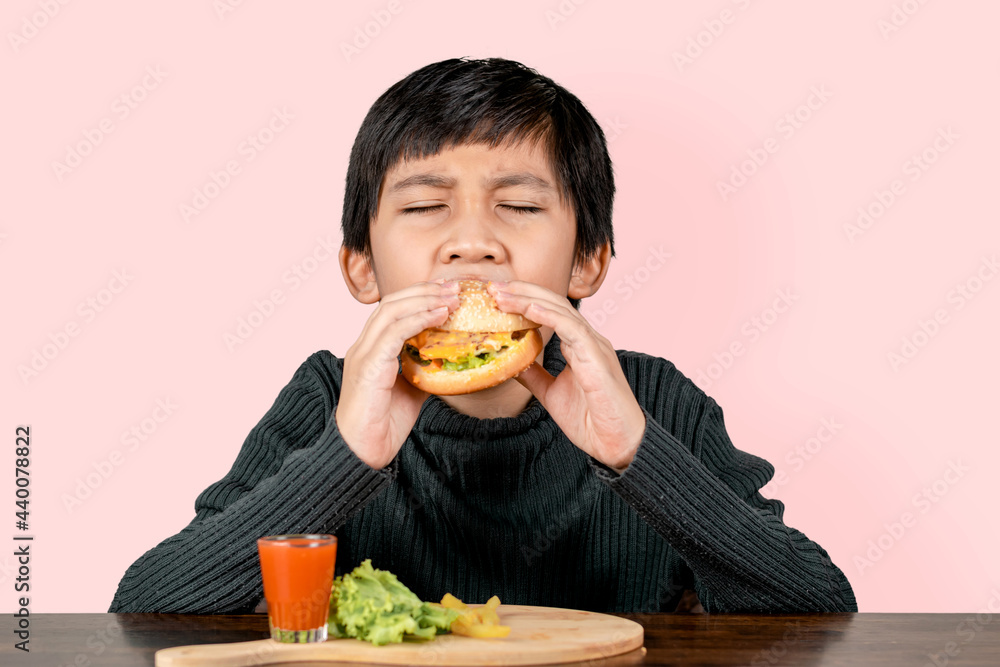 Cute Asian boy eating a delicious hamburger with happiness on pink background. Cute Asian boy eating a delicious hamburger with happiness on pink background.