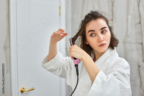 woman using a hair straightener in bathroom.