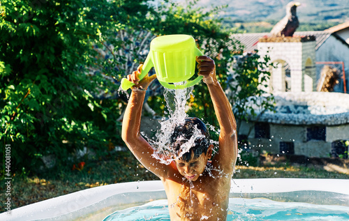 Caucasian child playing with water in an inflatable pool in the home garden at summer evening photo