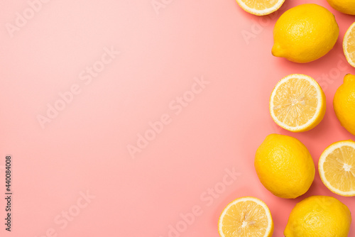 Top view photo of halves and whole yellow lemons on the right on isolated light pink background with copyspace on the left