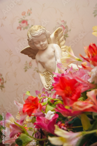 Fototapeta Naklejka Na Ścianę i Meble -  Lovely angel in flowers. Cherub sitting in the flowers of the daylily. Love symbol. Little angel figurine.
