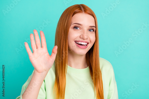 Photo of sweet funky young woman wear green shirt waving arm smiling isolated teal color background