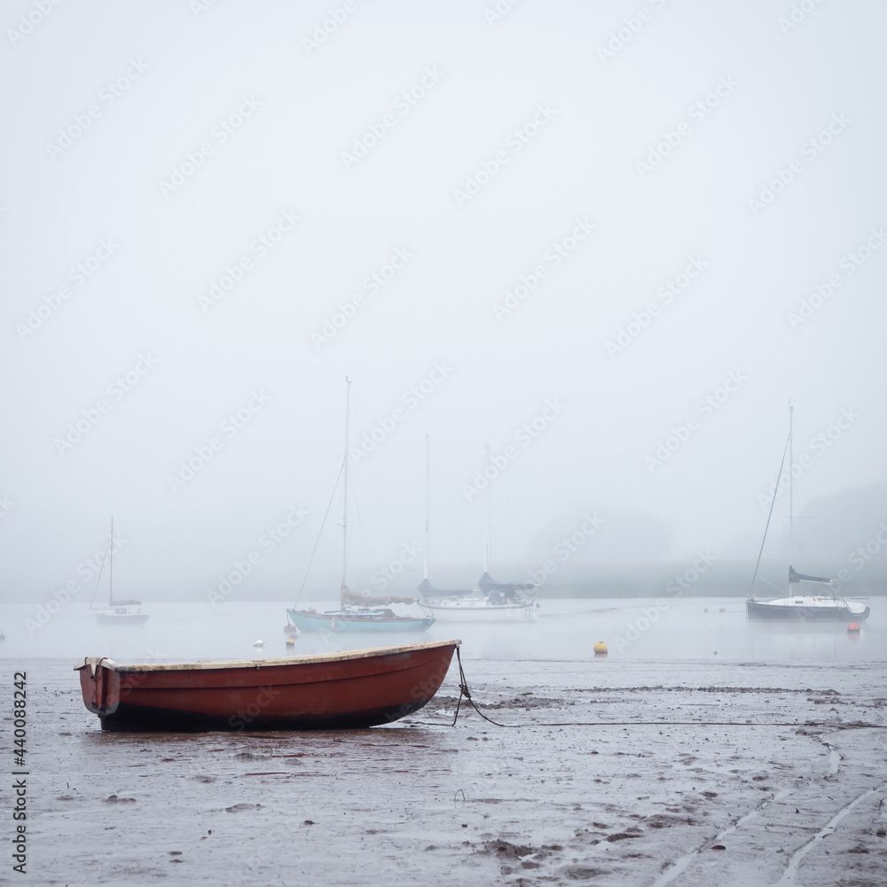 Small boats moored on the estuary at low tide as the fog rolls in