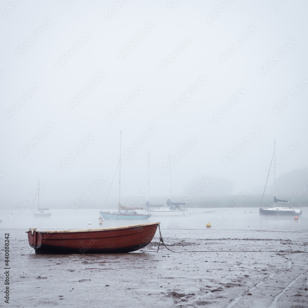 Small boats moored on the estuary at low tide as the fog rolls in Small boats moored on the estuary at low tide as the fog rolls in
