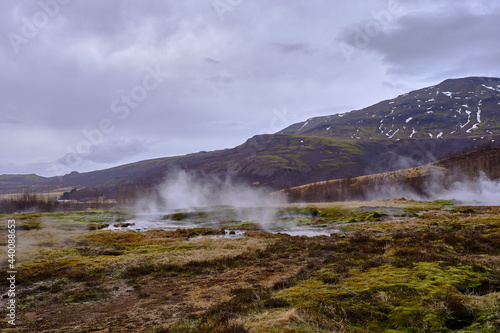 Steam pours out from the various mud puddles and vents all around Stokkur Geyser in Iceland and the surrounding landscape and mountains
