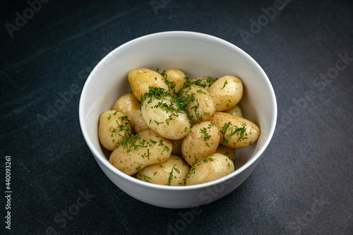 young boiled potatoes with butter, herbs on a dark table 