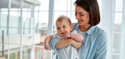 Loving mom carying of her newborn baby at home.Mom and baby boy playing in sunny bedroom. Parent and little kid relaxing at home. Family having fun together. Childcare, maternity concept.