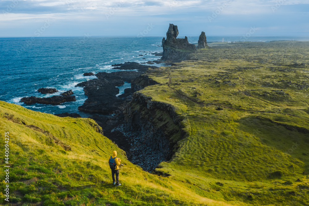 Man hiker in yellow jacket stand on the peak of the rock in outdoor park in Iceland. Londrangar