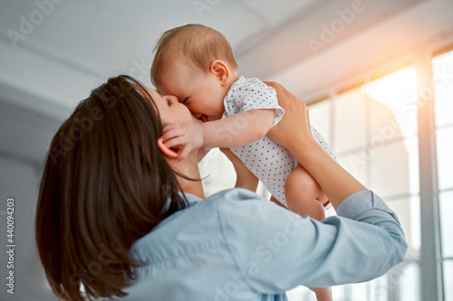 Loving mom carying of her newborn baby at home.Mom and baby boy playing in sunny bedroom. Parent and little kid relaxing at home. Family having fun together. Childcare, maternity concept. photo