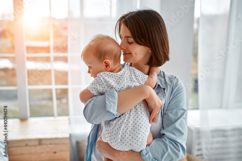 Loving mom carying of her newborn baby at home.Mom and baby boy playing in sunny bedroom. Parent and little kid relaxing at home. Family having fun together. Childcare, maternity concept.