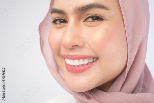 Portrait of young smiling muslim woman wearing a pink hijab over white background studio.