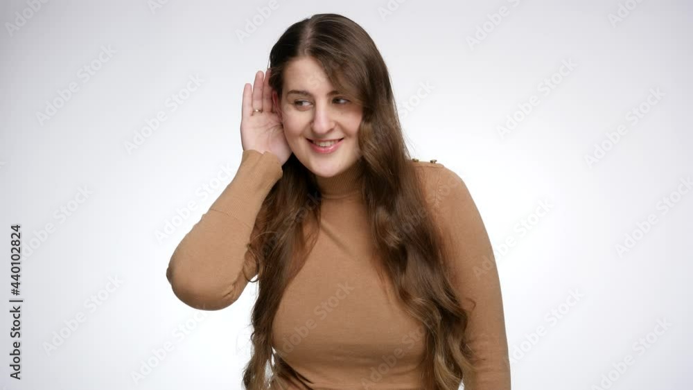 Studio portrait of smiling woman holding hand at ear and overhearing somebody talking. Concept of gossips, getting information and listening to secrets Studio portrait of smiling woman holding hand at ear and overhearing somebody talking. Concept of gossips, getting information and listening to secrets