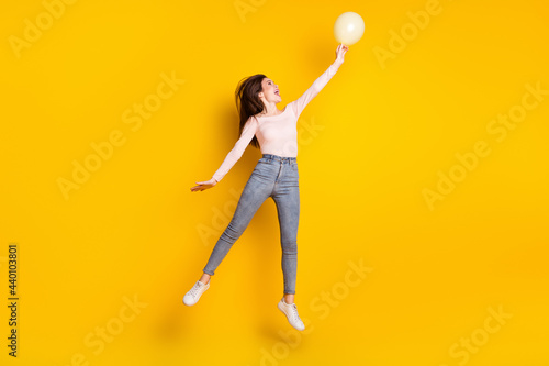 Full size profile side photo of young happy excited girl jumping look copyspace hold balloon isolated on yellow color background