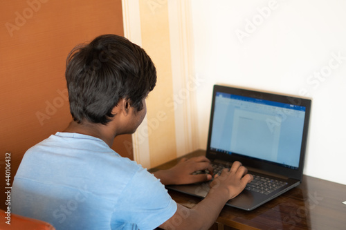 Portrait of a young Indian teen typing on laptop. Indian student uses laptop to complete his assignment. Online education concept. Kid typing on his laptop to complete his school project.	