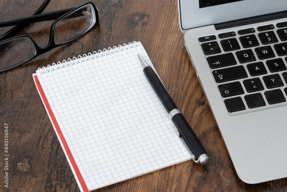 pen and blank spiral notepad with quad-rules paper next to laptop computer on wooden table pen and blank spiral notepad with quad-rules paper next to laptop computer on wooden table