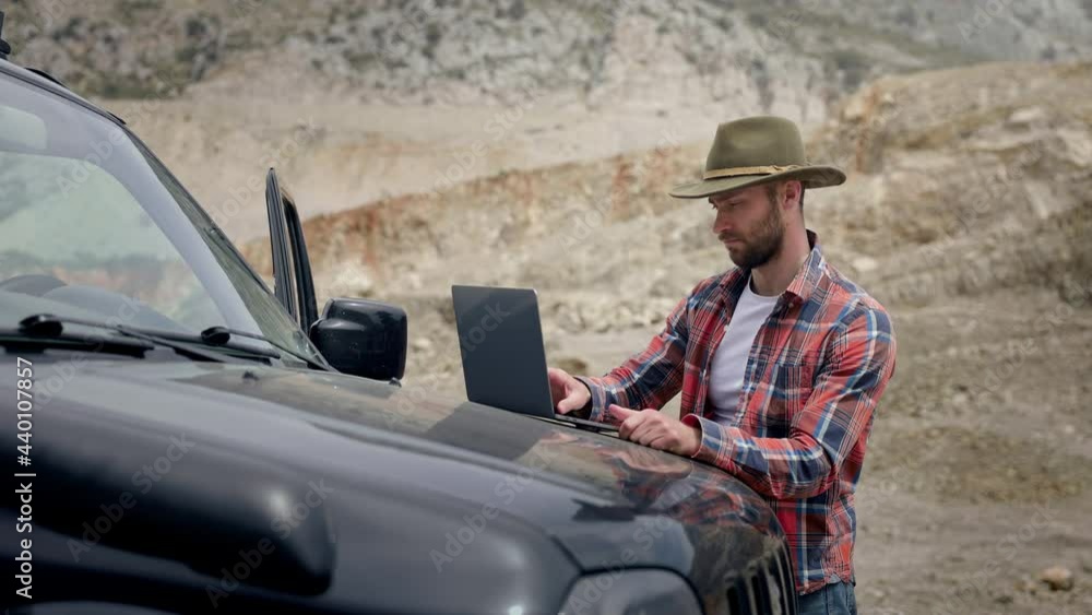 Man Working With Laptop On Car. Stylish Guy With Beard In Nature. Around Large Stones. Man Working With Laptop On Car. Stylish Guy With Beard In Nature. Around Large Stones.