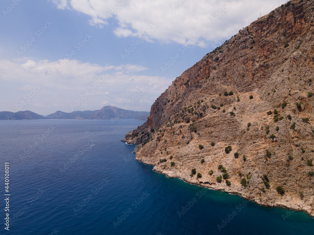 Fototapeta premium Turkish blue waters and sharp mountains near Oludeniz taken from drone on a partially cloudy summer day