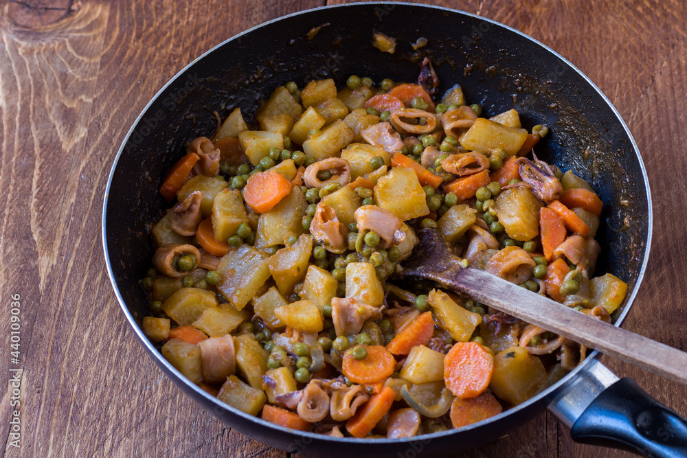 Squid with potatoes, peas and carrots cooked in a pan on wooden background Squid with potatoes, peas and carrots cooked in a pan on wooden background