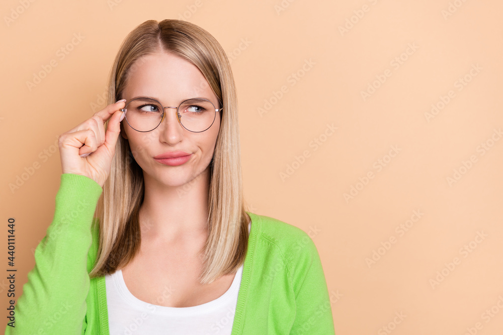 Portrait of attractive suspicious girl touching specs looking aside copy space solution isolated over beige pastel color background