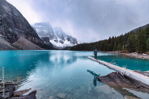Man traveler standing on timber with Rocky Mountains on gloomy in Moraine Lake at Banff National Park