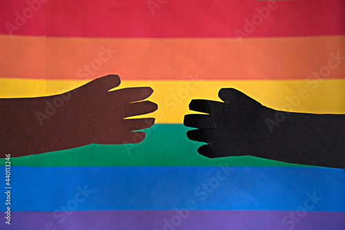 A couple of African ethnicity holding hands in front of a rainbow LGBTQIA flag