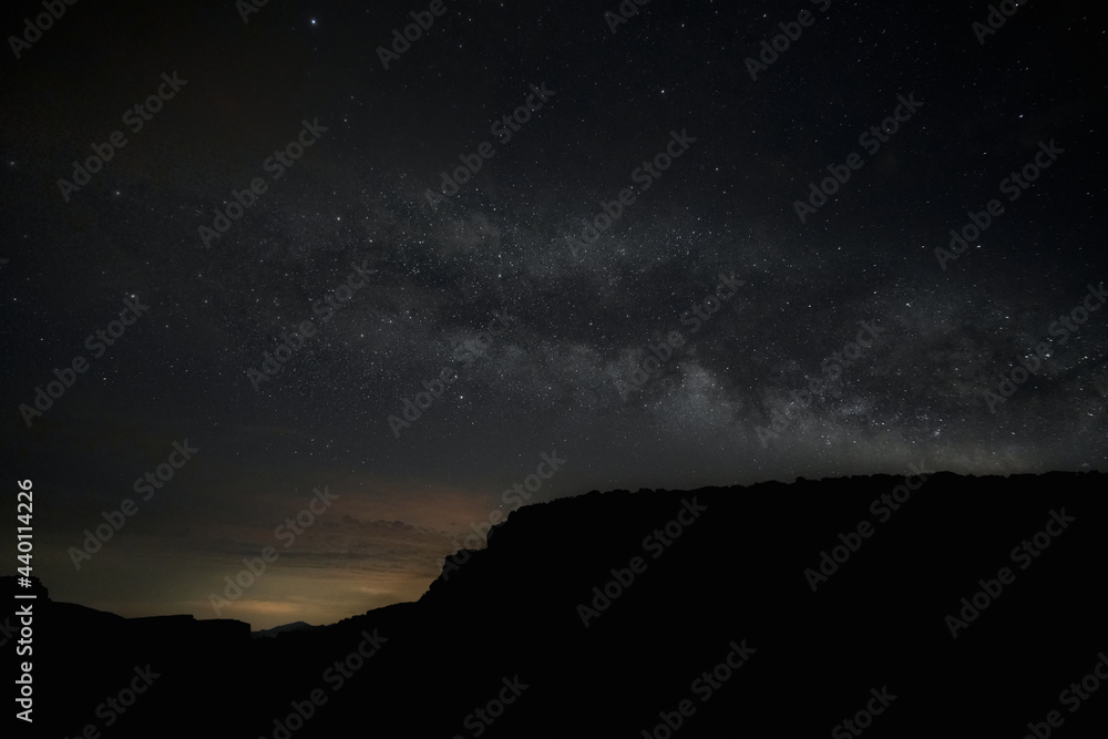 Starry sky view with the Milky Way in the middle. Moutains silhouettes over the dark and starry sky