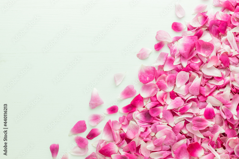 Pink rose petals placed in the corners on white wooden table with space for text in the center. Top view.