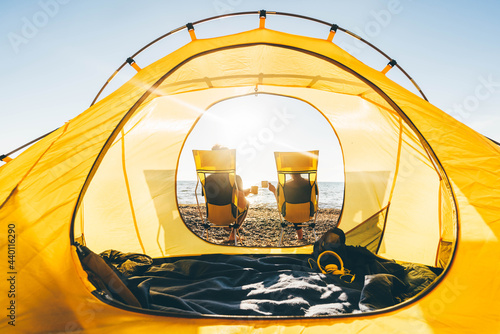 Couple relaxing at camping tent near the sea at sunset.