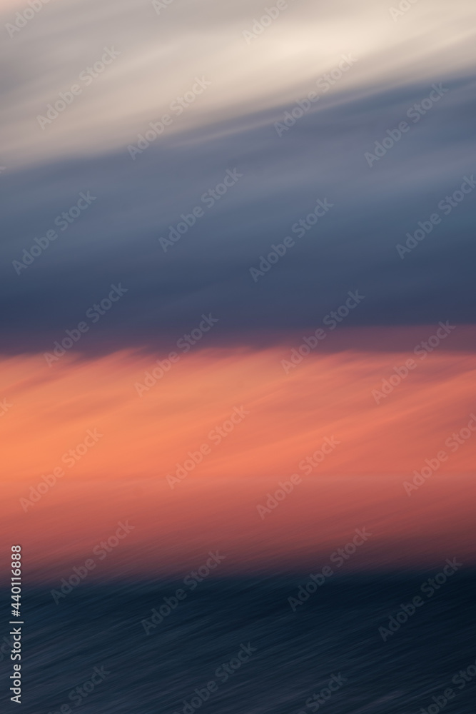 Long exposure of a sunset over a mountain range with long, sweeping clouds