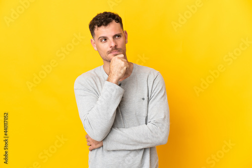 Young caucasian handsome man isolated on yellow background having doubts and thinking