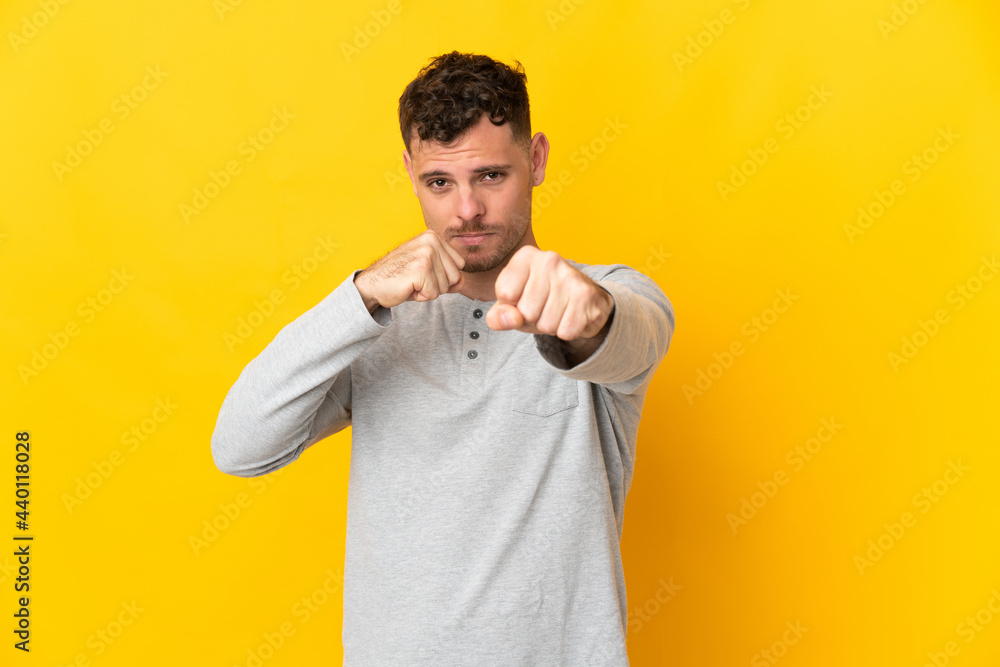 Young caucasian handsome man isolated on yellow background with fighting gesture Young caucasian handsome man isolated on yellow background with fighting gesture