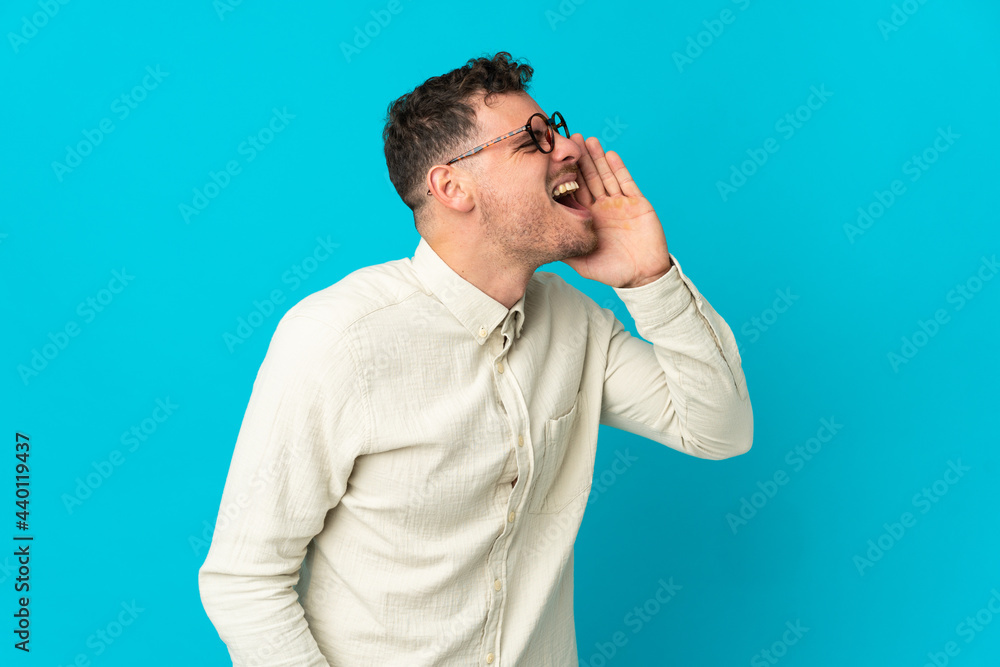 Young caucasian handsome man isolated on blue background shouting with mouth wide open to the side Young caucasian handsome man isolated on blue background shouting with mouth wide open to the side