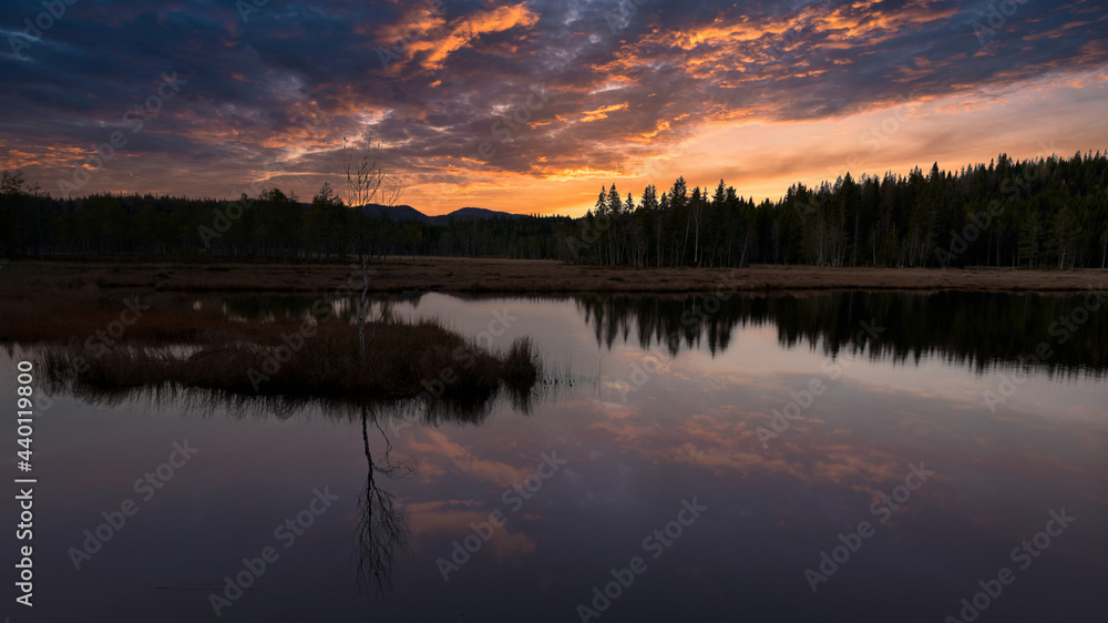 Fototapeta premium Sunset over the lake. The sky is dramatic and on fire. Shot in Nordmarka, Oslo, Norway. Triungtjerna or Triungsvann national park.
