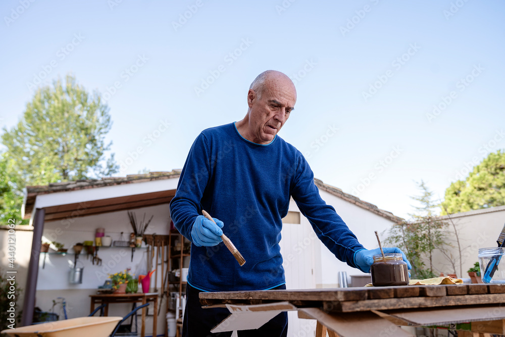 Active senior man painting wooden plank at back yard Active senior man painting wooden plank at back yard
