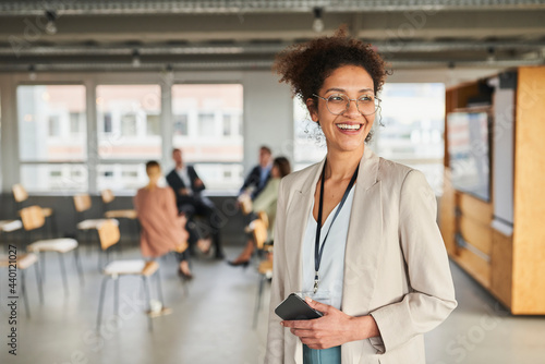 Smiling businesswoman with mobile phone looking away at office