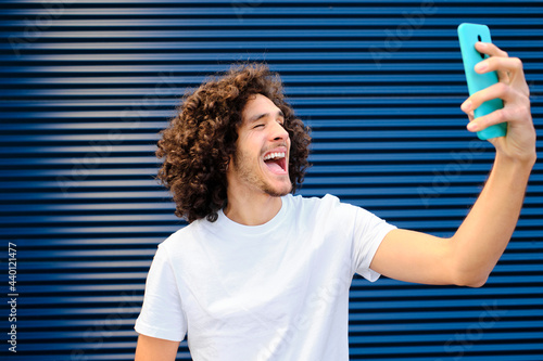Cheerful young man making face while taking selfie through mobile phone