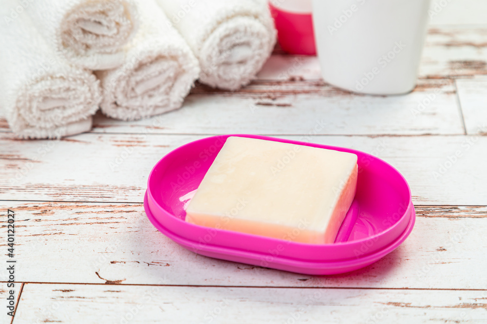 soap on pink plastic soap dish with towels on white wooden table in bathroom