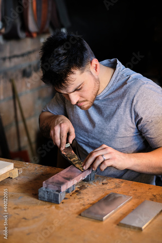 Male metal worker sharpening knife on table at workshop photo