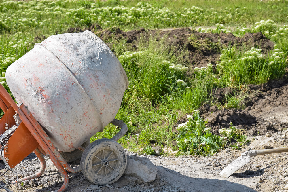 Mobile concrete mixer on background of pile of gravel. Preparatory work for preparation of concrete mass. Close-up. Selective focus. Mobile concrete mixer on background of pile of gravel. Preparatory work for preparation of concrete mass. Close-up. Selective focus.