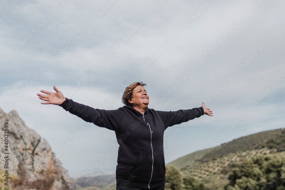 Carefree senior woman standing with arms outstretched on mountain Carefree senior woman standing with arms outstretched on mountain