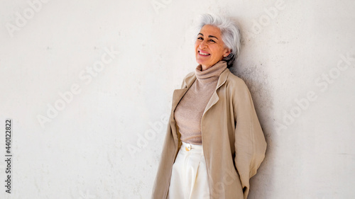 Smiling woman in trench coat leaning on wall