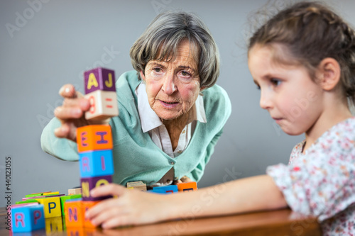 Senior woman stacking toy block while playing with girl at home photo