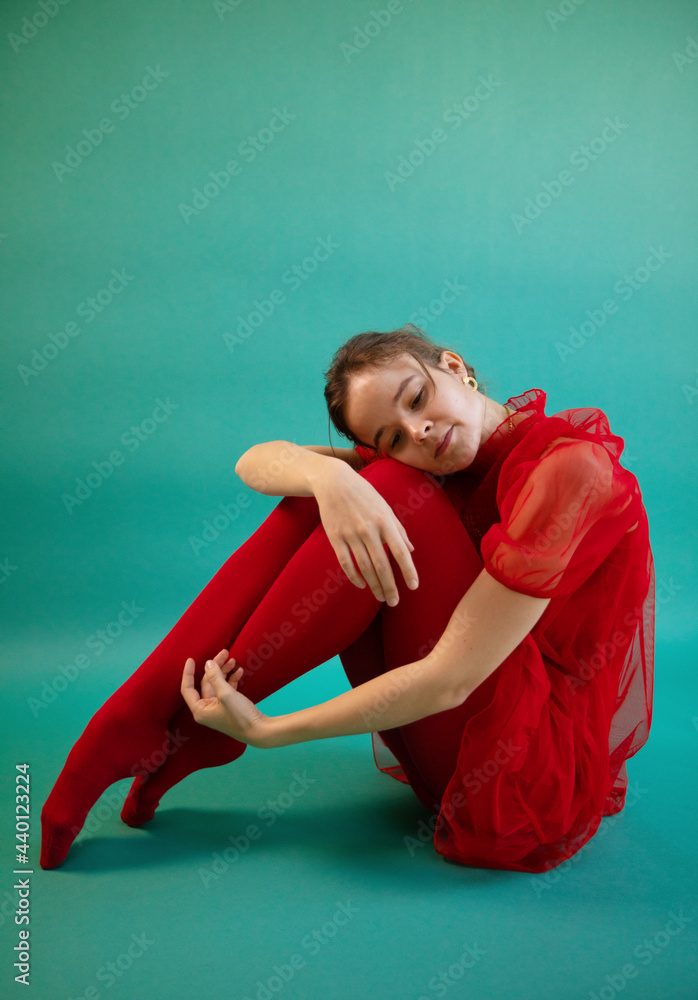 Young female dancer sitting on turquoise background Young female dancer sitting on turquoise background