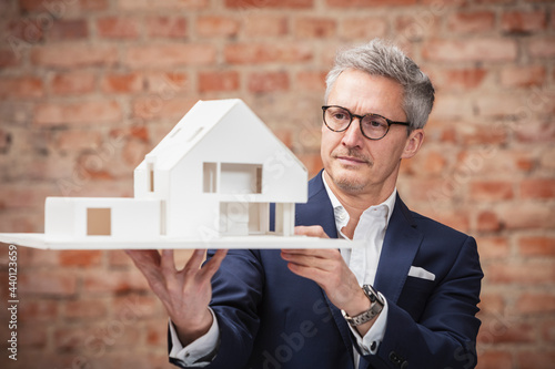 Mature businessman planning while looking at model house at work place photo