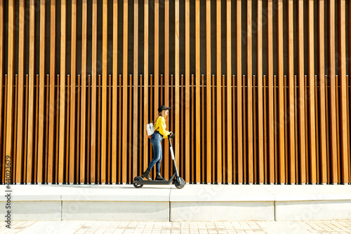 Young woman with backpack riding electric push scooter on sunny day photo