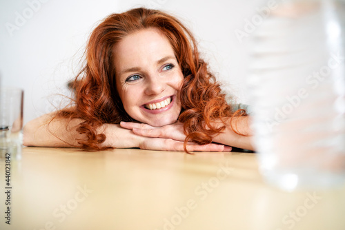 Thoughtful redhead woman leaning on table while looking away at home